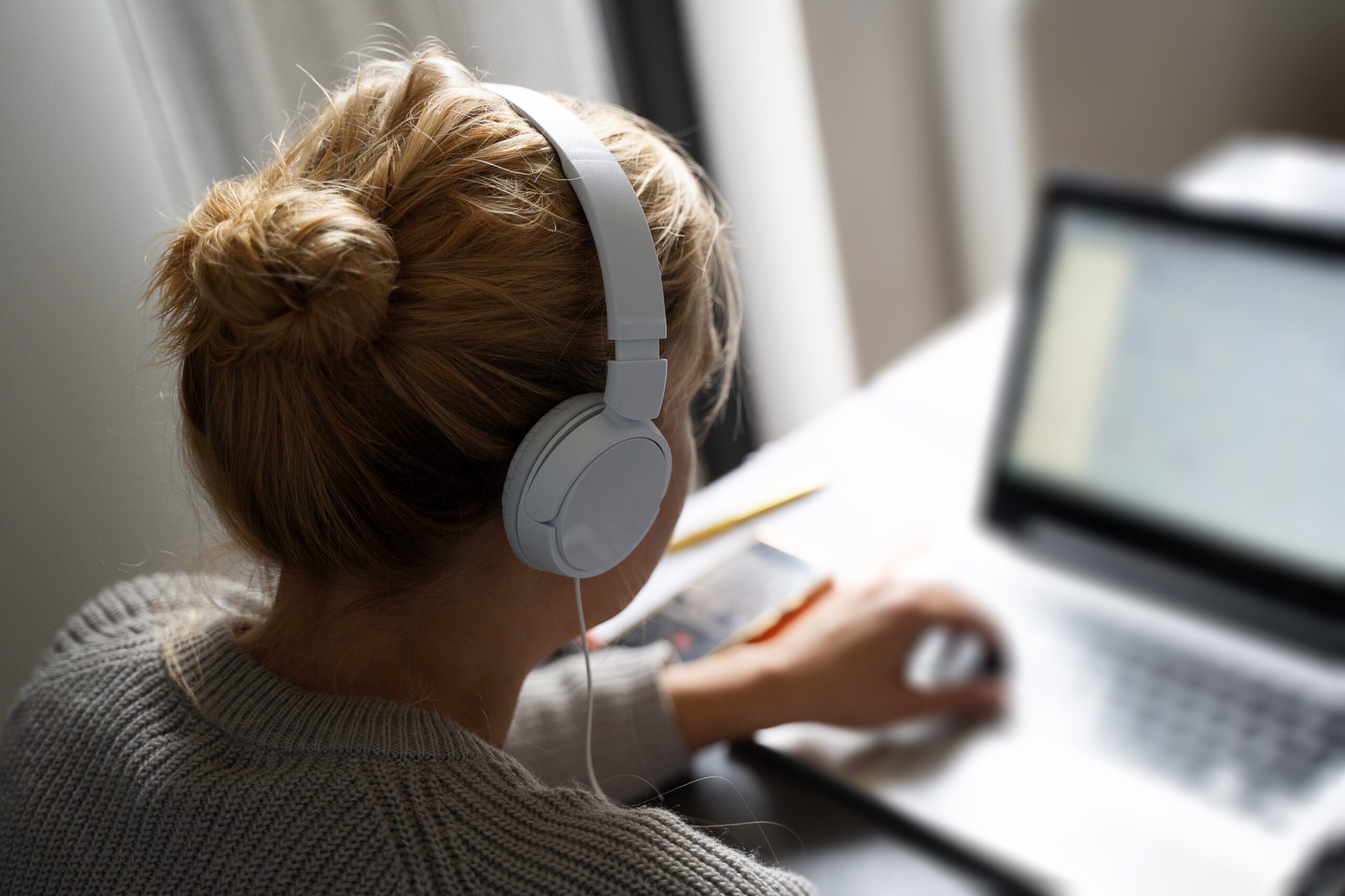 Woman wearing headphones working on a laptop.