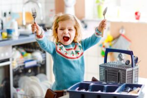 Toddler raising folk and spoon triumphantly in a kitchen