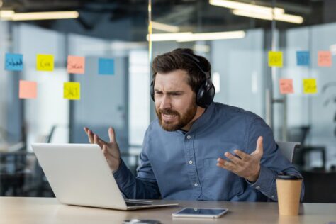 Confused man in headphones gesturing in frustration at his laptop