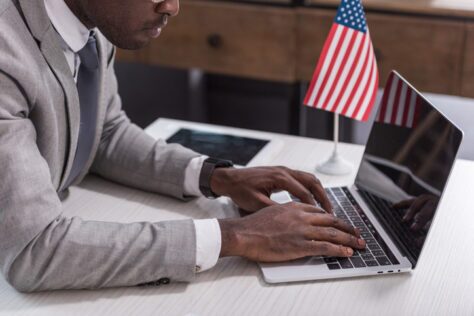 Man typing on a laptop with a small US flag on his desk, demonstrating digital accessibility lawsuits