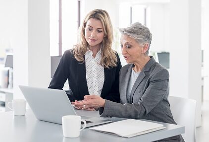 Two businesswomen in an office using laptop . Accessibility Fuels Search, UX, and Credibility