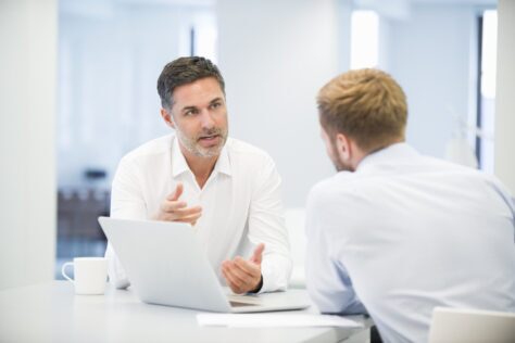 Two men conferring in an office over a laptop, discussing internal PDF accessibility