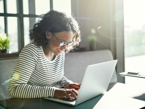 Woman smiling while working at her laptop in a sunny office.